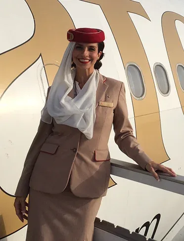 Larissa Belkis de uniforme da Emirates, encostada na escada de uma aeronave.